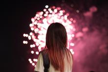 Girl watching a fireworks show as pink fireworks explode in the air